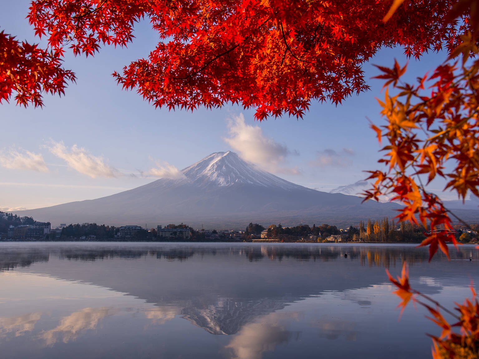 Mount Fuji and its reflection in Lake Kawaguchi, framed by red autumn maple leaves